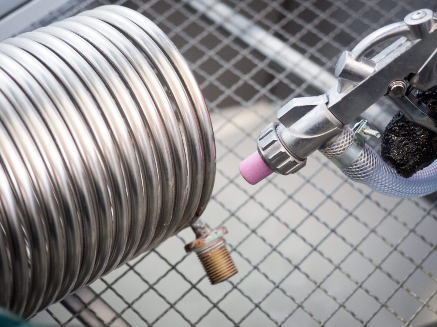 A metal spiral tube with a threaded end being sprayed by a nozzle on a grid-patterned surface.